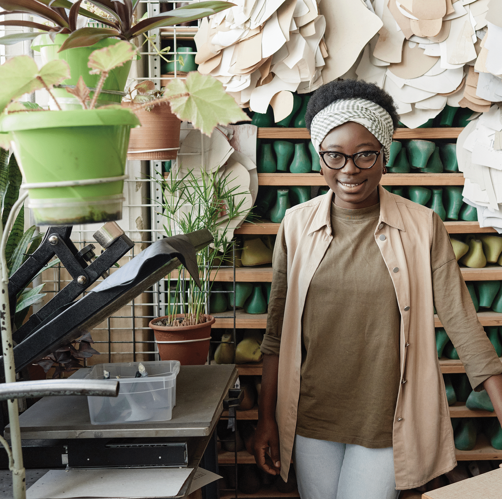 Portrait of African young shoemaker smiling at camera while standing in the workshop with shoelast on the shelves in the background